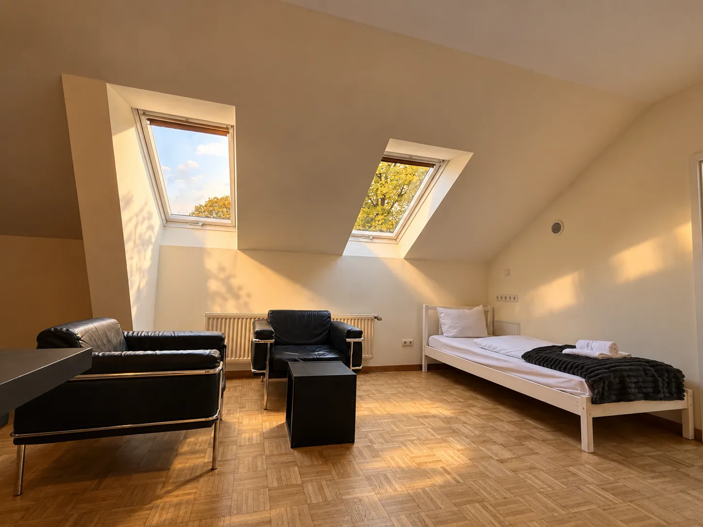 Einzelbett und Sitzgruppe unter Dachfenstern